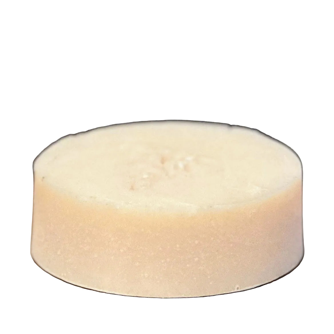 Round beige soap bar on a wooden surface with a keyboard in the background